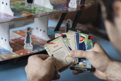 Mężczyzna trzymający w dłoniach karty do gry. W tle plansza ułożona w model statku.