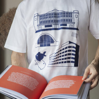 Mężczyzna czytający książkę. Ma na sobie białą koszulkę z czterema granatowymi grafikami. Na grafikach: budynek Muzeum Emigracji, Polskich Linii Oceanicznych, Hali Targowej i pomnik gdyńskich rybek.