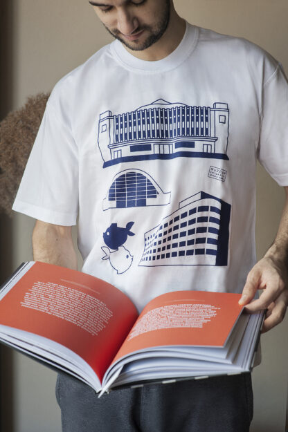 Mężczyzna czytający książkę. Ma na sobie białą koszulkę z czterema granatowymi grafikami. Na grafikach: budynek Muzeum Emigracji, Polskich Linii Oceanicznych, Hali Targowej i pomnik gdyńskich rybek.