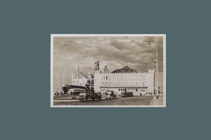Czarno-białe zdjęcie Dworca Morskiego w Gdyni. Przed budynkiem samochody, a po jego lewej stronie statek pasażerski.